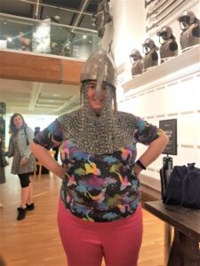 A women wearing pink trousers an a blue patterned top. She is wearing an early piece of head amour.