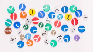 Bottle caps of lots of different colours and size, all with different white lines on them. Some lines are in a V shape whilst others are in a Y shape and others are just squiggly lines