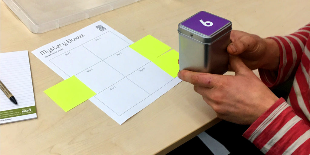 Person holding one of the Mystery Boxes, shaking it to get some ideas as to what is in it and writing down what they observe.